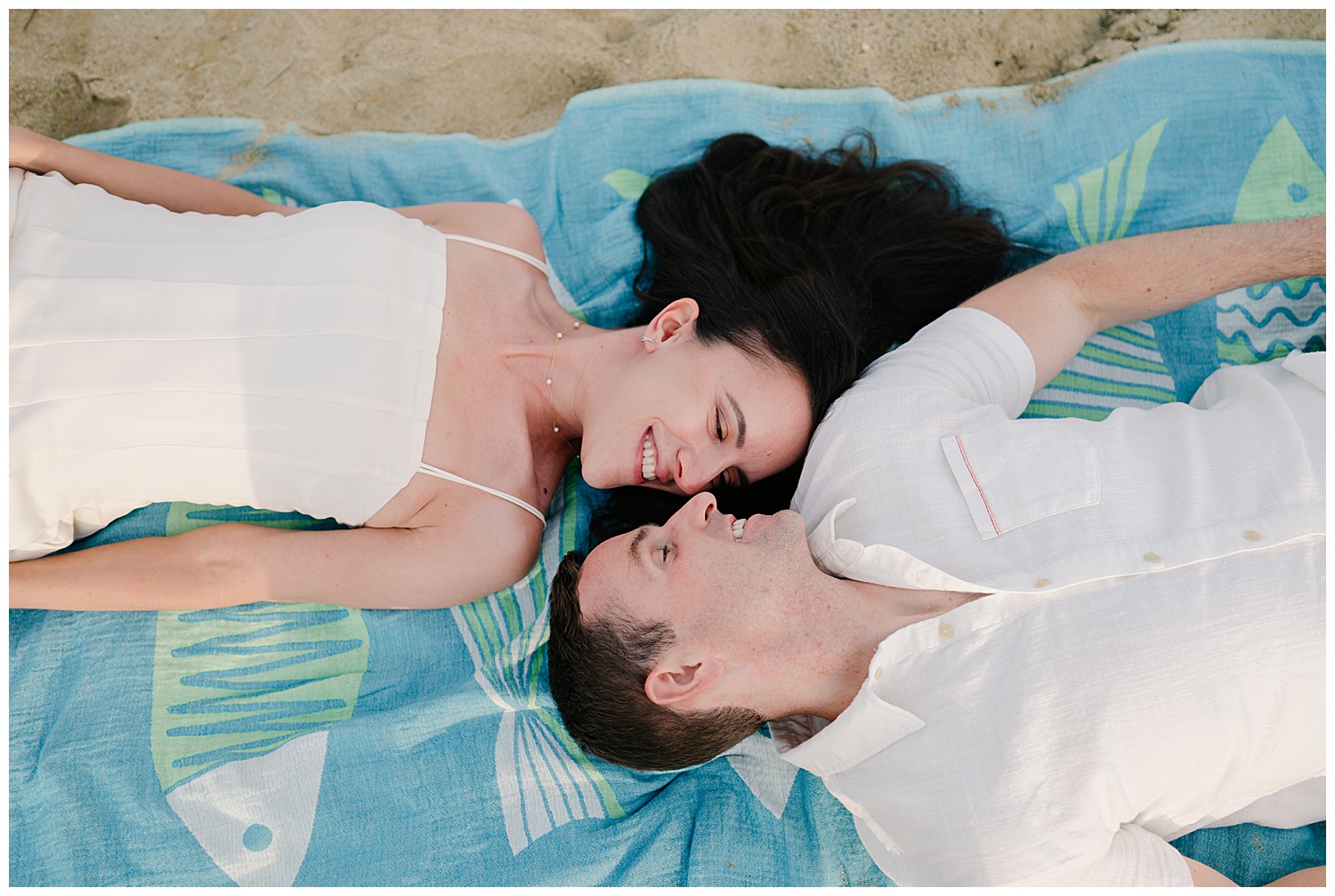 couple laying on a blanket on the beach smiling at each other